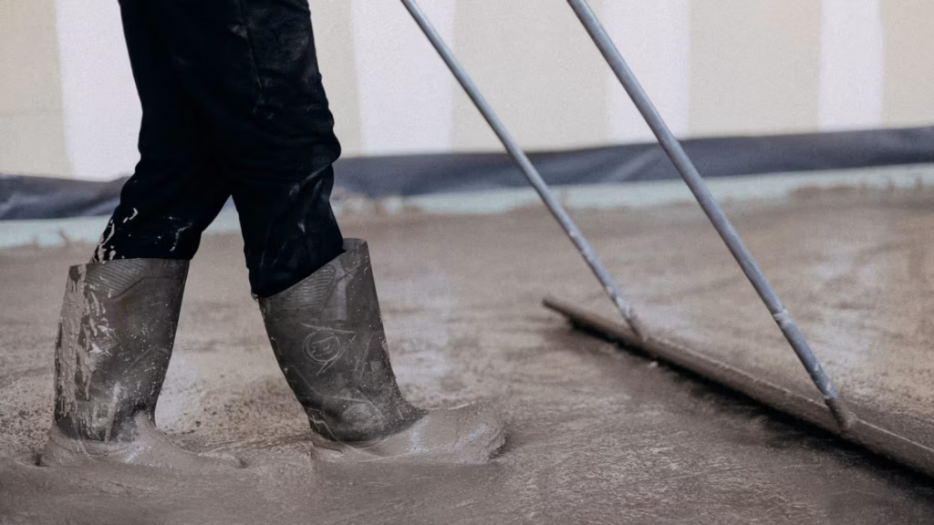Chapiste en bottes égalisant une chape liquide fraîche à la barre de lissage